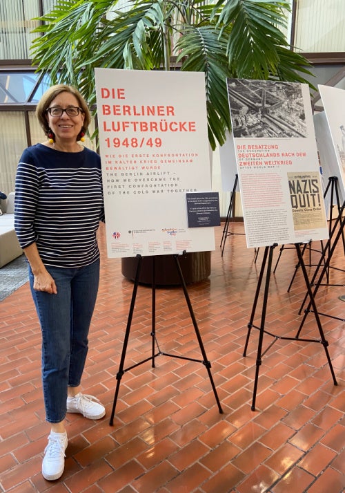 Professor Anja Banchoff stands in the ICC Galleria with the Berlin Airlift posters on easels next to her.