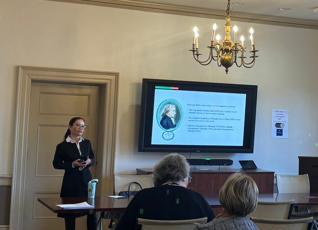 Dr. Huaping Lu-Adler stands behind the desk during her presentation on November 15. An image of Immanuel Kant is on the TV screen next to her. 